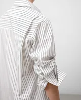 Camisa de algodón orgánico, blanca con finas rayas verticales negras. Presenta un corte oversize, cuello solapa, manga larga con puño y bolsillo en el pecho.
