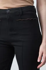 Pantalón de fit recto color beige, confeccionado en cotton spandex. Presenta costuras visibles y bordados decorativos en tono dorado/marrón claro. El ruedo del pantalón tiene un borde festoneado.