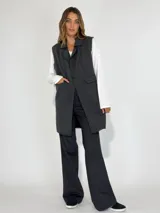 Chaleco largo color beige, con cuello solapa, un botón frontal y dos bolsillos de parche. Presenta costuras decorativas en contraste.