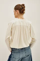 Remera de algodón color crudo, con cuello en V y mangas largas. Presenta un diseño holgado con puños tejidos y detalle de costura central en el escote.