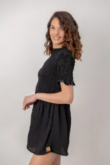 Vestido corto de color negro, con cuerpo y mangas cortas de nido de abeja fruncido, y falda corta con vuelo.