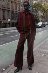 Pantalón de tiro alto color bordó, con pinzas delanteras, bolsillos frontales y falsos bolsillos con solapa en la espalda. Tiene pernera ancha y cierre frontal con cremallera, botón interior y gancho.