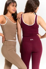 Conjunto deportivo compuesto por una musculosa con escote redondo y vivos blancos, y un pantalón de corte recto con cintura cruzada en V. Ambas prendas son de color habano y presentan el logo bk. estampado en blanco.