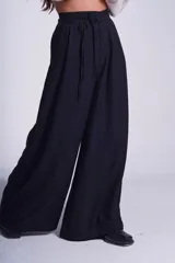 Pantalón negro de corte sastrero con tablas frontales y cintura con lazo. Diseño de pierna ancha y tiro alto.