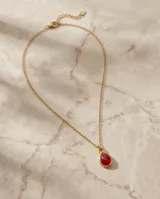 Collar de acero con baño de oro, compuesto por una cadena fina de eslabones y un dije en forma de gota con piedra roja central.