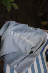 Sweater de punto color celeste con cuello redondo y mangas largas. Presenta la inscripción 'JOSE IGNACIO' tejida en color blanco en el frente y cuenta con puños y ruedo acanalados.