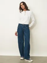 Jean de corte recto y tiro medio, con un acabado de lavado oscuro y efecto de textura sutil en la tela. Presenta cierre frontal con botón y bolsillos clásicos.