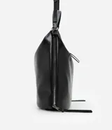 Cartera tipo hobo de gran tamaño confeccionada en poliuretano color negro, con acabado liso y brillante. Presenta un diseño de media luna con cierre superior de cremallera, correa de mano fija y asa larga desmontable. Incluye un detalle de cremallera lateral que permite expandir su capacidad interna.