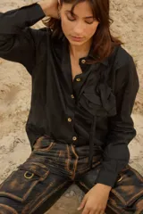 Camisa holgada blanca con detalle de roseta de tela en el frente, cuello camisero, botones a tono y diseño ligeramente más largo en la parte trasera.