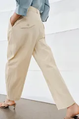 Pantalón de tiro medio confeccionado en algodón, con diseño cruzado en la cintura y cierre frontal con botones. Presenta trabillas para cinturón, bolsillos laterales ocultos y un bolsillo frontal con solapa y botón.