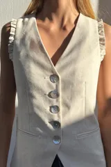 Chaleco largo color crudo confeccionado en lino, con escote en V, botones de nácar y volados en los hombros. Diseño entallado.