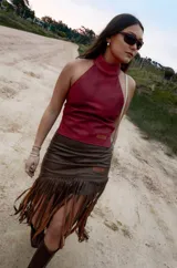 Pollera midi de cuero marrón con diseño asimétrico y flecos largos que aportan movimiento y textura.