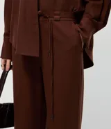 Pantalón sastre de corte wide leg en tejido crepé color marrón chocolate. Presenta una silueta recta y fluida, con cintura elástica y lazo ajustable para un calce cómodo.