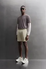 Short de running 2 en 1 color beige, confeccionado en tejido técnico ligero y elástico con malla interior integrada. Presenta cintura elástica ajustable con cordón, bolsillo trasero con cierre y aberturas laterales en el bajo.