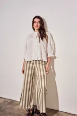 Blusa de algodón peinado color off-white, con cuello mao, cierre frontal de botones, mangas tres cuartos abullonadas con puños con volados, detalles de alforzas y apliques de encaje en el frente y los hombros.