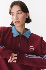 Buzo estilo rugby de corte oversized, color verde oscuro, con cuello tipo camisa en denim azul claro y cierre frontal parcial. Presenta un recorte horizontal en el pecho, logo bordado y tiras laterales en las mangas en contraste.