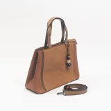 Cartera tipo tote color camel, con paneles laterales de textura granulada y panel central de tejido con textura diagonal. Incluye doble asa de mano, correa larga ajustable y extraíble, cierre superior y un dije colgante decorativo con cuentas de madera y piedra.