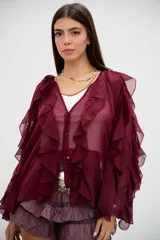 Blusa bordó de tela semitransparente con diseño de volados verticales en el frente y mangas largas acampanadas. Presenta cierre frontal con botones y detalles de bordados circulares sutiles en la parte inferior.