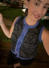 Chaleco tejido sin mangas, color negro, con textura brillante (lurex) y ribetes en azul. Presenta un escote redondo y se ata al frente con cordones.