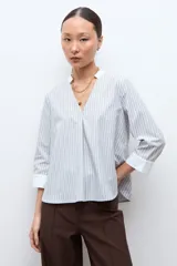 Blusa rayada en tonos beige y celeste, con cuello mao, escote en V y mangas 3/4 con puños blancos.
