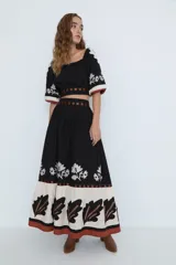 Top corto negro con escote bardot, mangas cortas abullonadas con bordado floral blanco y detalle de recortes con tiras horizontales color café en la cintura.