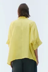 Camisa oversize blanca de lino, con corte cuadrado, mangas raglán cortas con puños anchos, aberturas laterales y cierre frontal de botones.