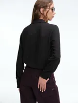 Camisa negra de manga larga con cuello clásico y detalle de volados en la parte frontal. Confeccionada en una mezcla de viscosa y lana virgen.