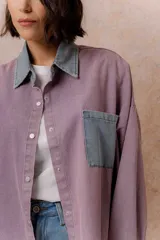 Camisa lila de calce relajado y manga larga, con cuello clásico, puños y bolsillo delantero en denim contrastante. Cierre frontal con broches metálicos.