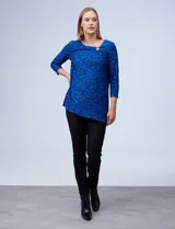 Blusa azul con estampado de círculos negros, de tejido texturado con escote en V descentrado y aplique de aro metálico.