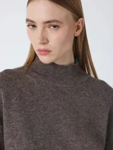 Suéter de cuello alto, color beige topo, de manga larga y calce holgado. Presenta un borde de punto acanalado en el cuello, puños y bajo, con una camisa de rayas negras y beige asomando por el bajo.