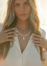 Collar corto de cristalitos facetados blancos, con dije colgante de pez dorado y detalles metálicos en acero dorado.