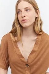 Remera marrón de tejido liso, con escote en V, mangas cortas y cierre frontal con botones.