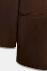 Blazer de mujer color marrón oscuro, con cuello solapa, manga larga y un solo botón de cierre frontal. Presenta bolsillos de vivo en el delantero.