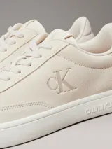 Zapatillas urbanas Calvin Klein modelo Classic Cupsole, color crema, con capellada de cuero gamuzado, interior de espuma, forro de malla de poliéster y suela de TPR. Presentan cordones, detalle de pala vega, lengüeta trasera acolchada y logo CK en el lateral.
