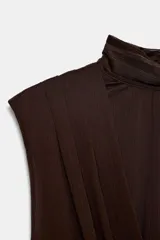 Vestido corto de cuello subido y diseño sin mangas, con cuerpo superior cruzado y falda con detalle de frunces laterales. Cuenta con forro interior y cierre lateral con cremallera oculta.