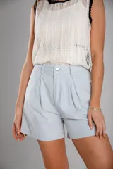 Short de gabardina color celeste claro, tiro alto, con pliegues frontales y cierre de botón metálico.