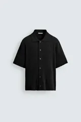 Camisa relaxed fit de punto tejida en hilatura con mezcla de algodón, color negro, con cuello solapa, manga corta y cierre frontal de botonadura.