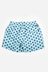 Short de baño celeste con estampado de hojas pequeñas en tonos verdes y blancos. Cuenta con cintura elástica con cordón ajustable, bolsillos laterales y un parche circular con logo en la parte inferior.