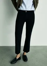 Jeans Alex de tiro medio confeccionados en denim negro, con diseño flare de corte acampanado y bajo deshilachado. Presenta cuatro bolsillos, incluyendo bolsillos frontales aplicados, y cierre frontal con cremallera y botón metálico.