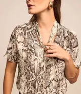 Blusa de chiffon con estampado de serpiente en tonos beige y marrón. Tiene cuello alto con lazo y mangas cortas.