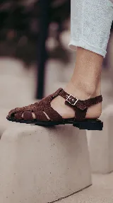 Sandalia cangrejera color chocolate, confeccionada 100% en cuero, con tiras entrelazadas, base de goma flexible y hebilla lateral ajustable.