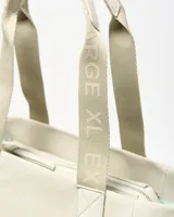 Cartera tipo tote color beige con asas de hombro decoradas con el texto impreso de la marca, bolsillo frontal y parche circular grabado con el logotipo en la parte inferior.