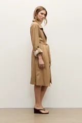 Trench de lyocell color beige con solapas amplias, cierre cruzado con botones, bolsillos laterales y mangas largas con presillas en los puños que permiten ajustarlas.