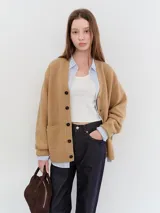 Cardigan de punto color camel, de corte relajado y silueta boyfriend, con cuello redondo, cierre frontal de botones oscuros y bolsillos frontales.