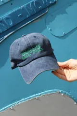 Gorro de visera de tela color gris desgastado, con bordado frontal en hilo rojo que dice "COSTA DULCE" y un diseño de ondas o símbolos repetidos encima.