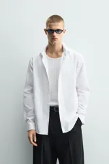Camisa de corte slim fit confeccionada en tejido de algodón con textura. Presenta cuello italiano, manga larga con puños abotonados y cierre frontal mediante botonadura.