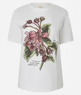 Remera blanca de algodón, corte slim fit, con cuello redondo y manga corta. Presenta un estampado bordado de flores rosadas y frutos con hojas verdes, acompañado de un pequeño texto en la parte inferior.
