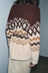 Chaqueta de punto con escote en pico y manga larga, confeccionada en tejido jacquard con diseño geométrico. Presenta detalles de lentejuelas y abalorios, cierre frontal con botones y un cinturón fino ajustable en la cintura.