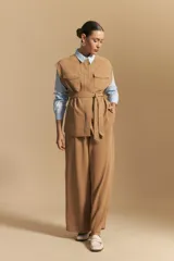 Chaleco negro de corte estructurado con cuello redondo, cierre frontal oculto y lazo ajustable en la cintura. Presenta dos bolsillos frontales con solapa y diseño de hombros caídos.