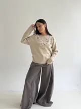 Sweater de punto color beige con cuello redondo, manga larga y detalle de bordado floral en la parte superior del pecho.